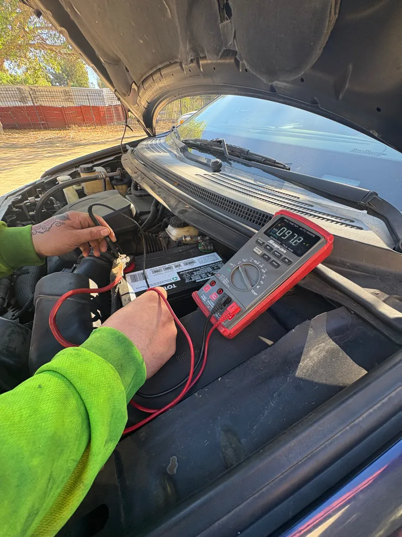 Mechanic in a high-visibility jacket testing battery voltage with a multimeter under an open hood