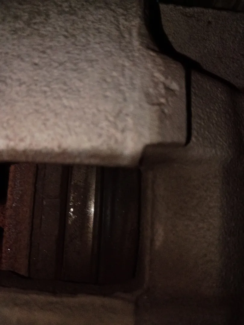 Close view of a brake caliper and worn brake pad against a rusted rotor edge