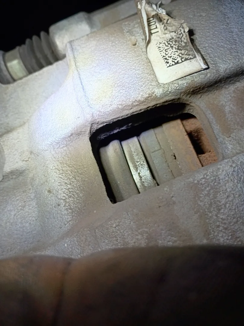 Brake caliper inspected with a flashlight showing remaining friction material on the pad through the caliper window
