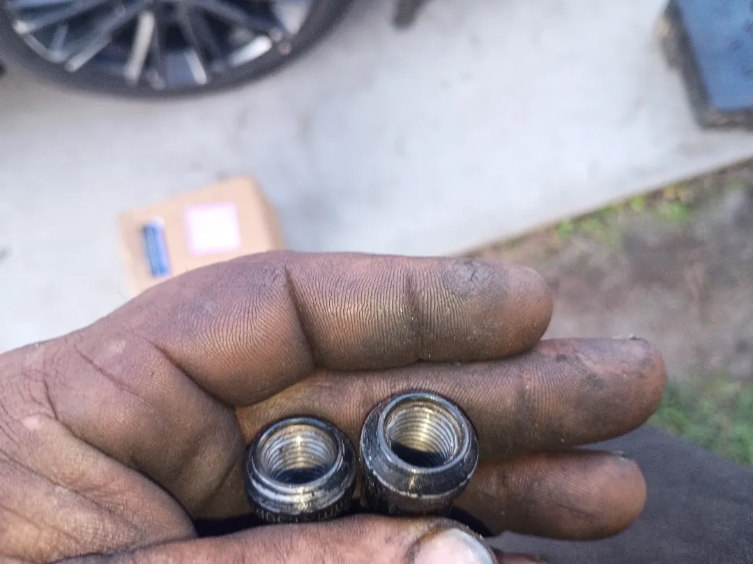 Mechanic's hand holding two brake caliper guide pin bushings removed from a vehicle