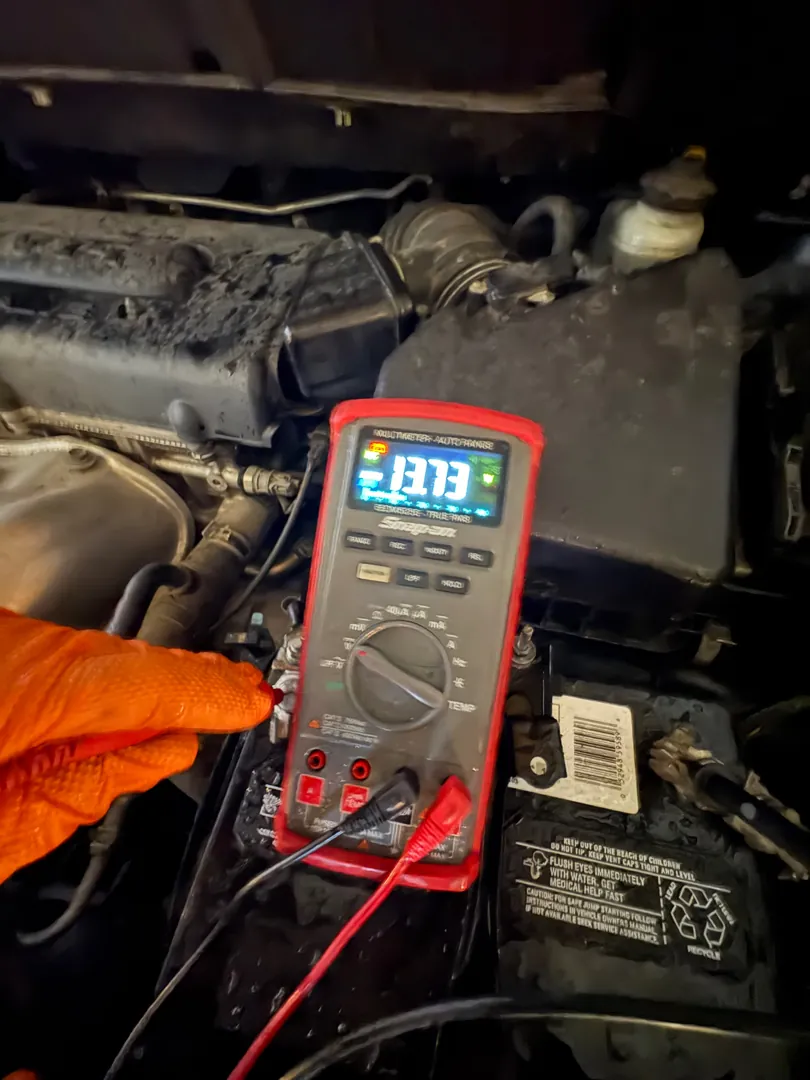 Digital multimeter in an engine bay reading 13.13 volts during an alternator test