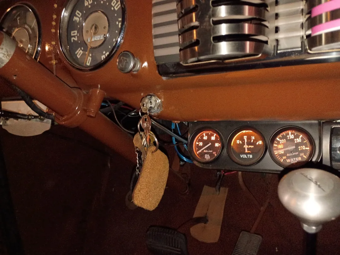 Interior of a vintage pickup showing an orange painted dash with aftermarket amp, volt and temperature gauges