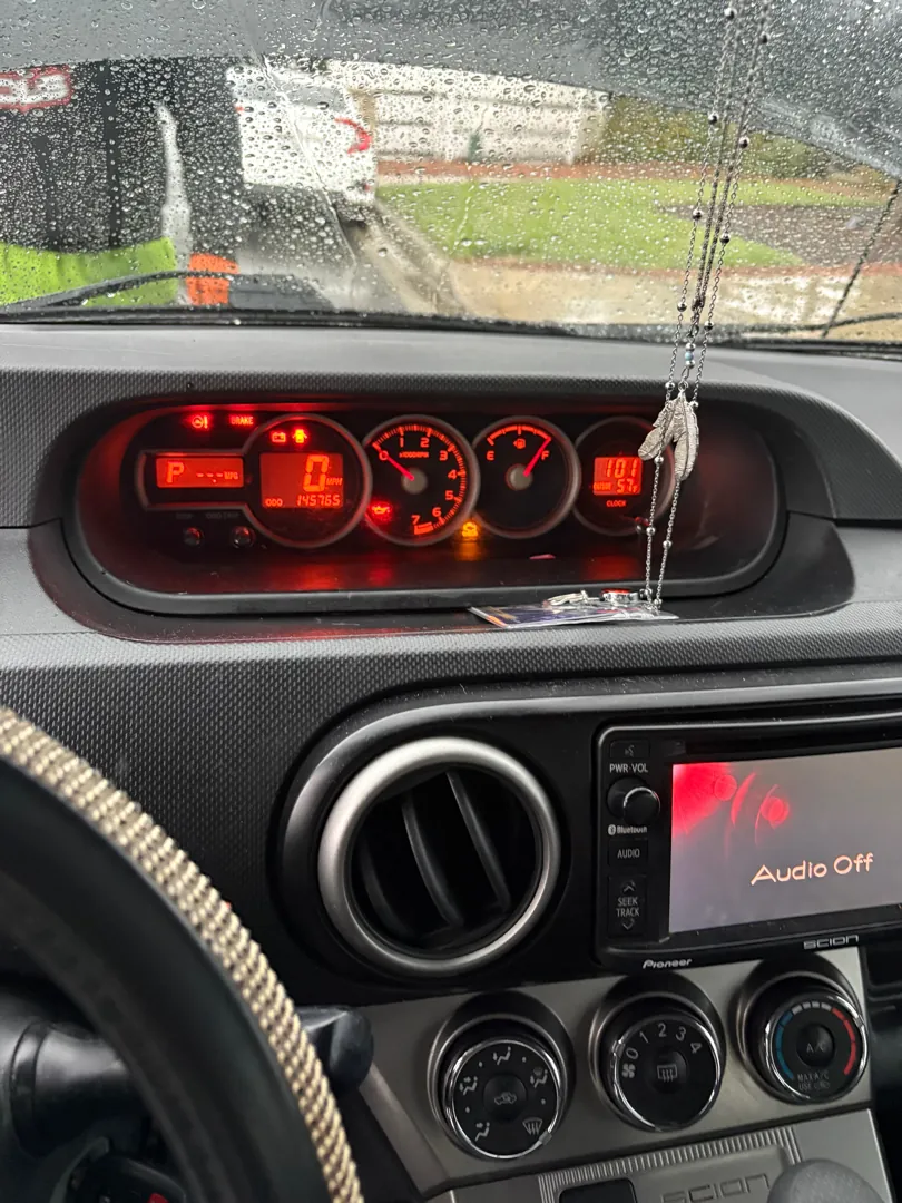 Car instrument cluster glowing at night with warning indicators while rain sits on the windshield