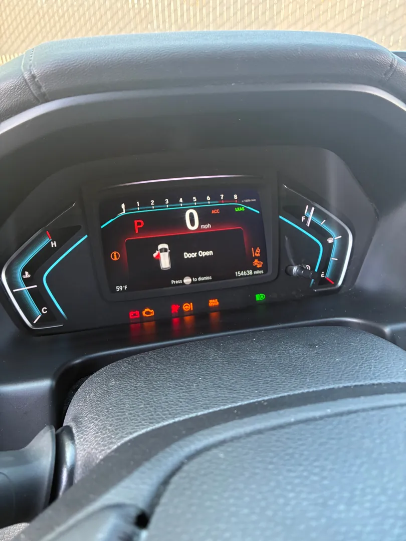 Digital instrument cluster of a minivan lit with a door open message and a row of warning indicators