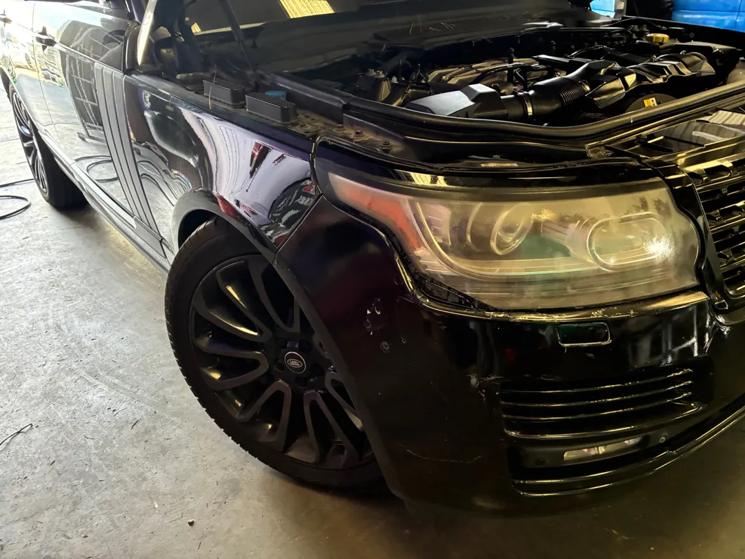 Front of a black Range Rover with the hood open in a workshop during an engine repair