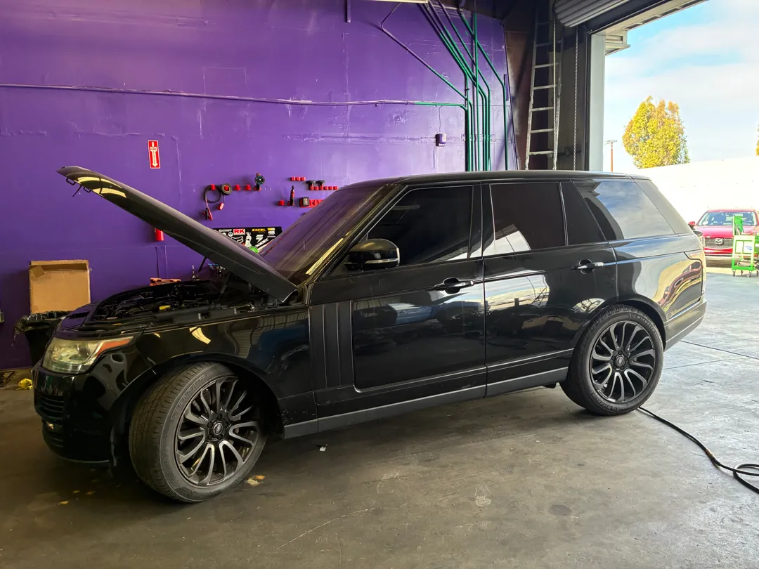 Black Range Rover with its hood raised inside a workshop bay during supercharger work