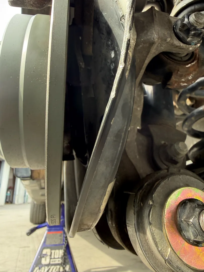 View inside a wheel well showing the brake rotor, strut and lower control arm with the wheel removed