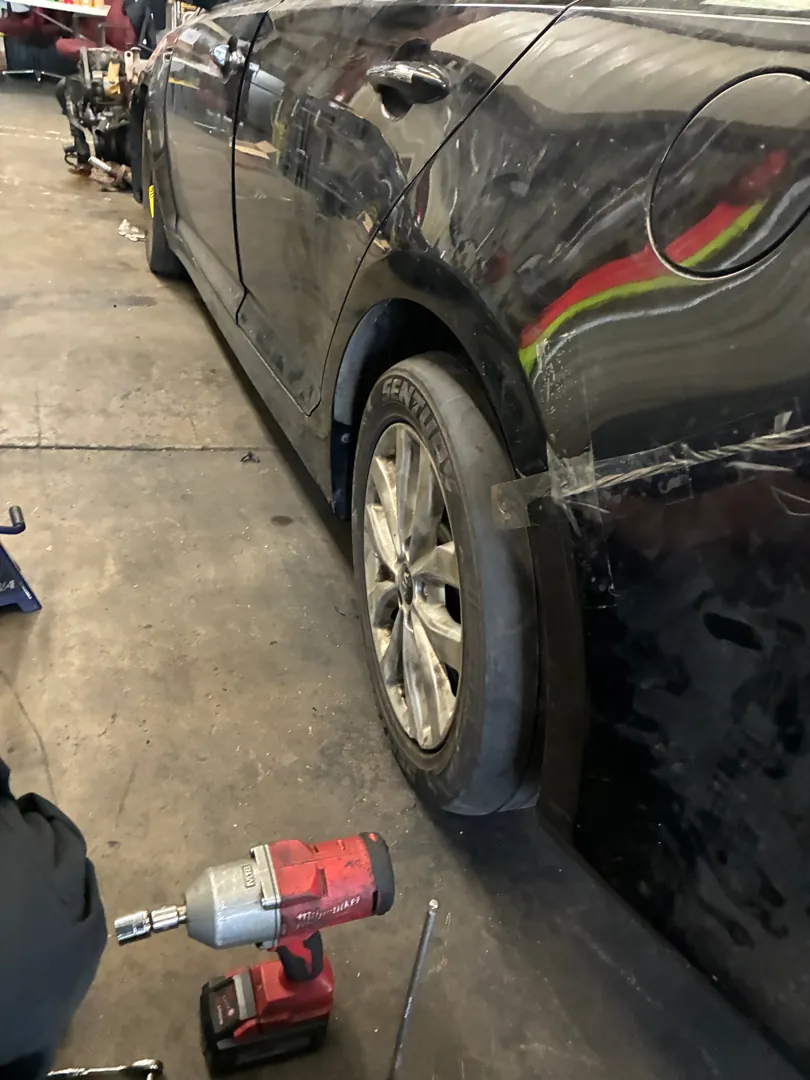 Sedan raised on jack stands with a cordless impact wrench on the ground during suspension work