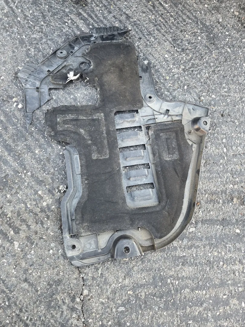 Engine splash shield removed from a vehicle and laid on the ground, coated in road grime