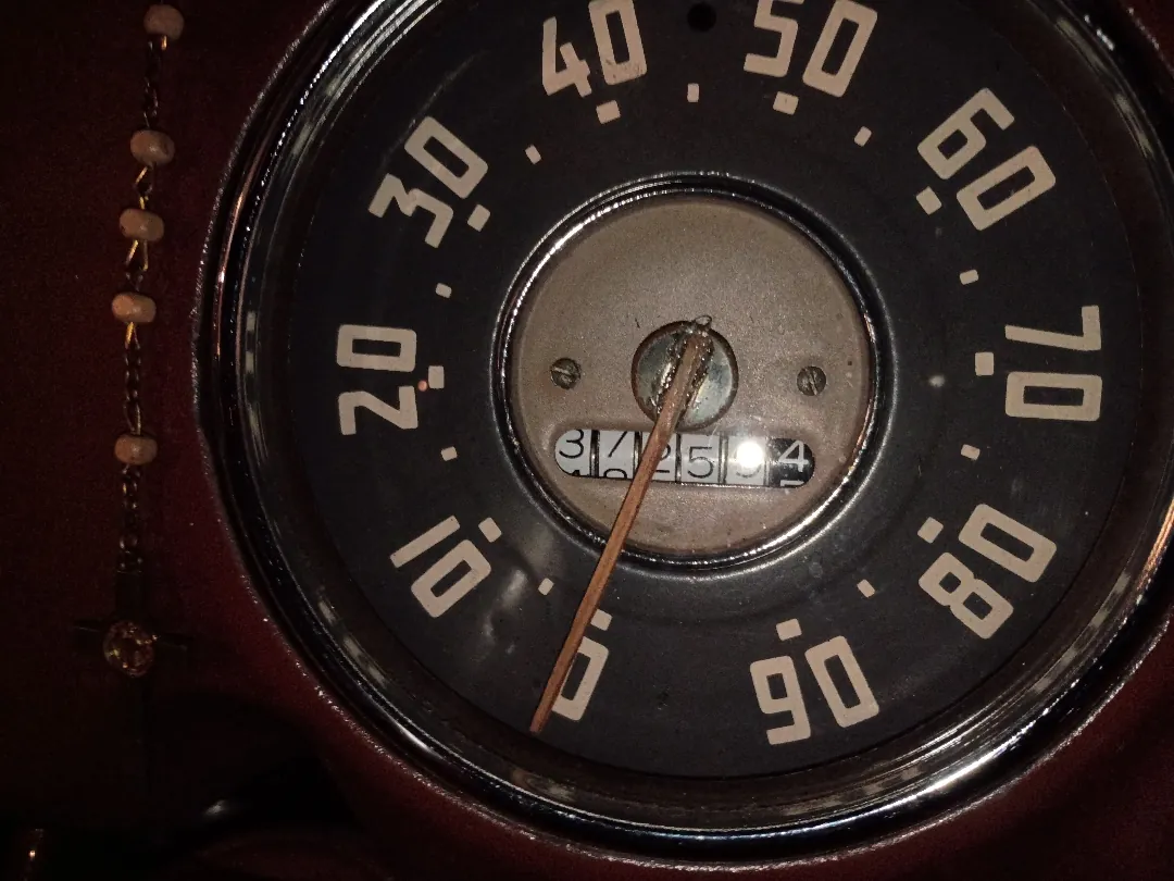 Round vintage speedometer face reading to 90 miles per hour with a mechanical odometer below it